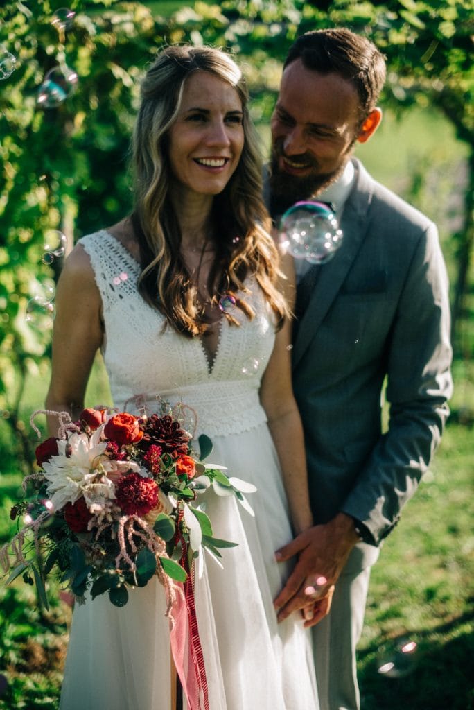 Hochzeitsfotografie_Kärnten_Zaunschirm_hochzeit babsi stefan1_Brautpaar mit Brautstrauß und Seifenblasen in den Weinbergen